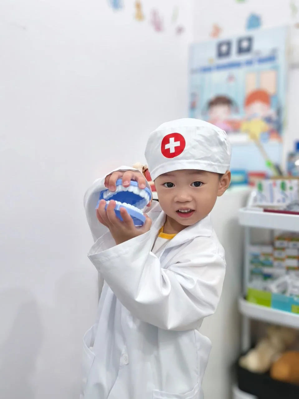 Young patient dressed up as a dentist holding a tooth model, showing how we make first dental visits fun and free of fear
