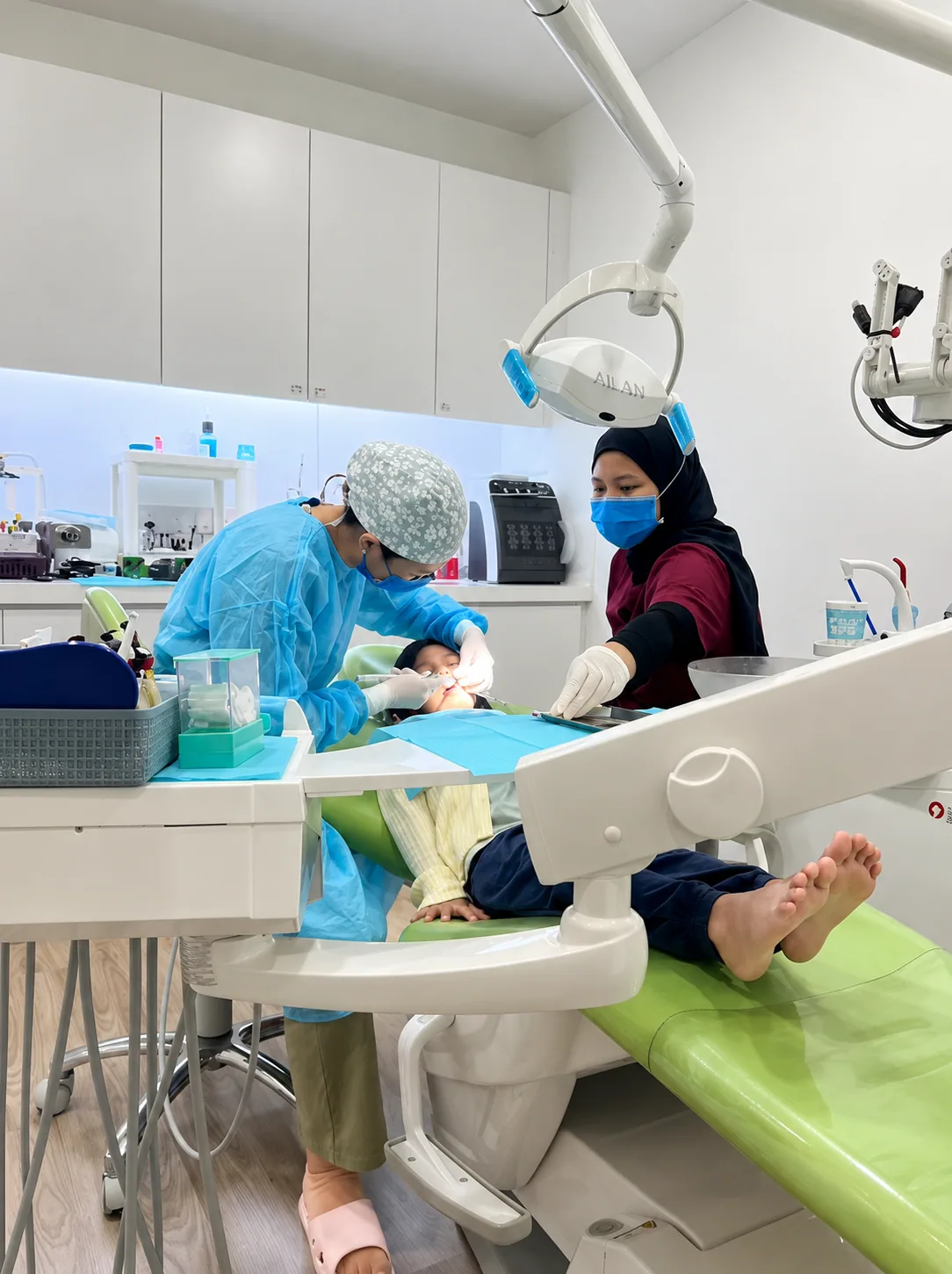 Dentist and assistant treating a patient in a fully equipped surgery room with modern chair and overhead lighting in Bukit Jalil