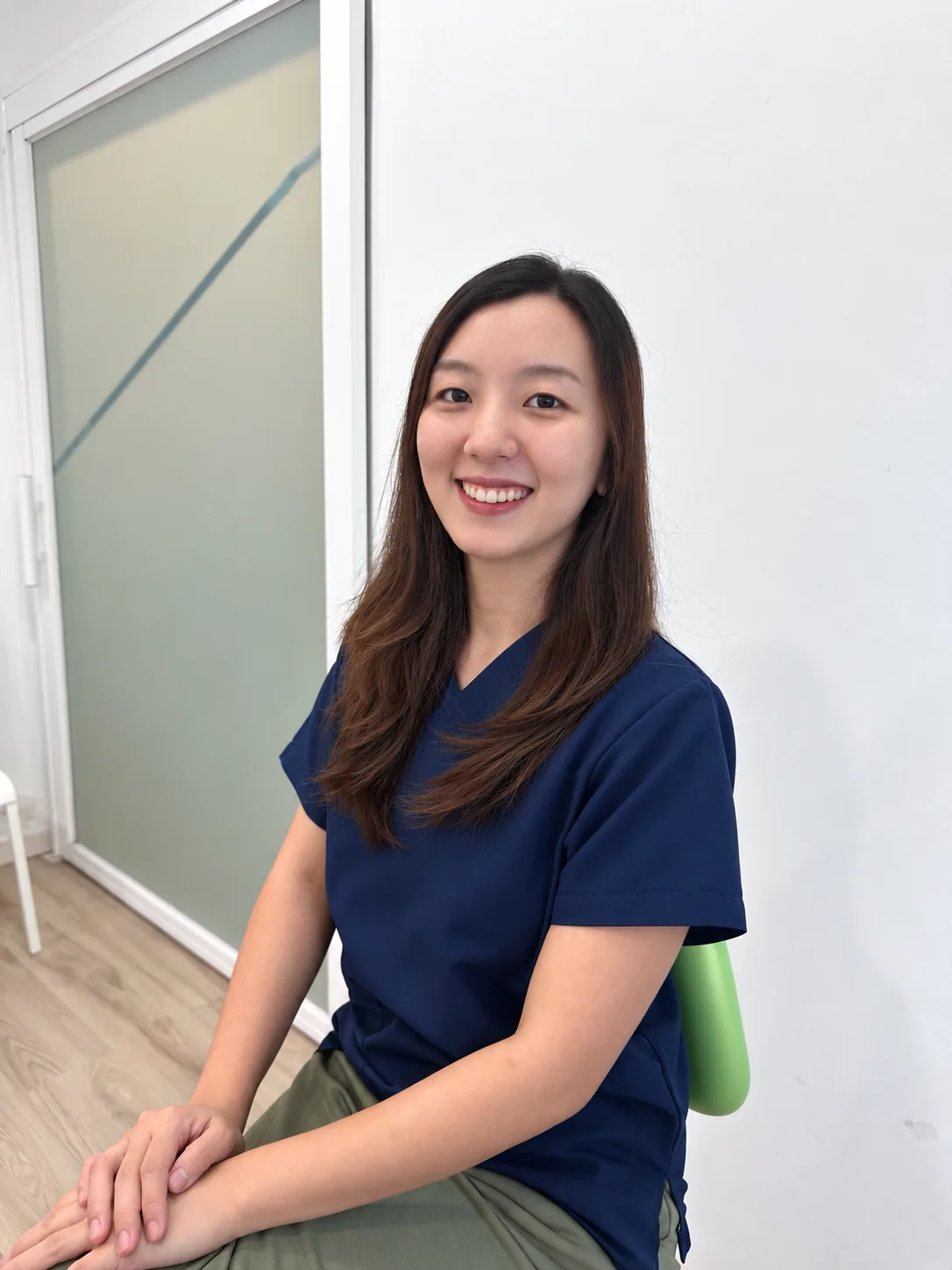 Dr. Khoo Cher Xing, resident dental surgeon at Lau & Su Partners Dental Bukit Jalil, smiling in navy scrubs in the clinic corridor