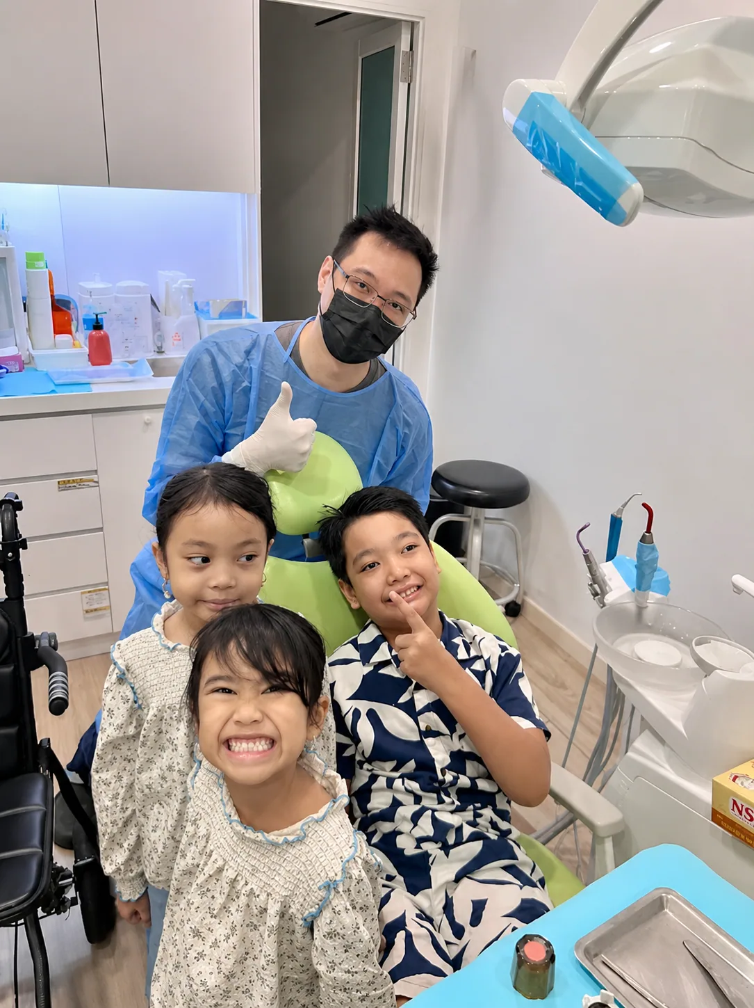 Dentist giving a thumbs up with three smiling children after their dental check-up, showing how gentle kids dentistry builds confidence