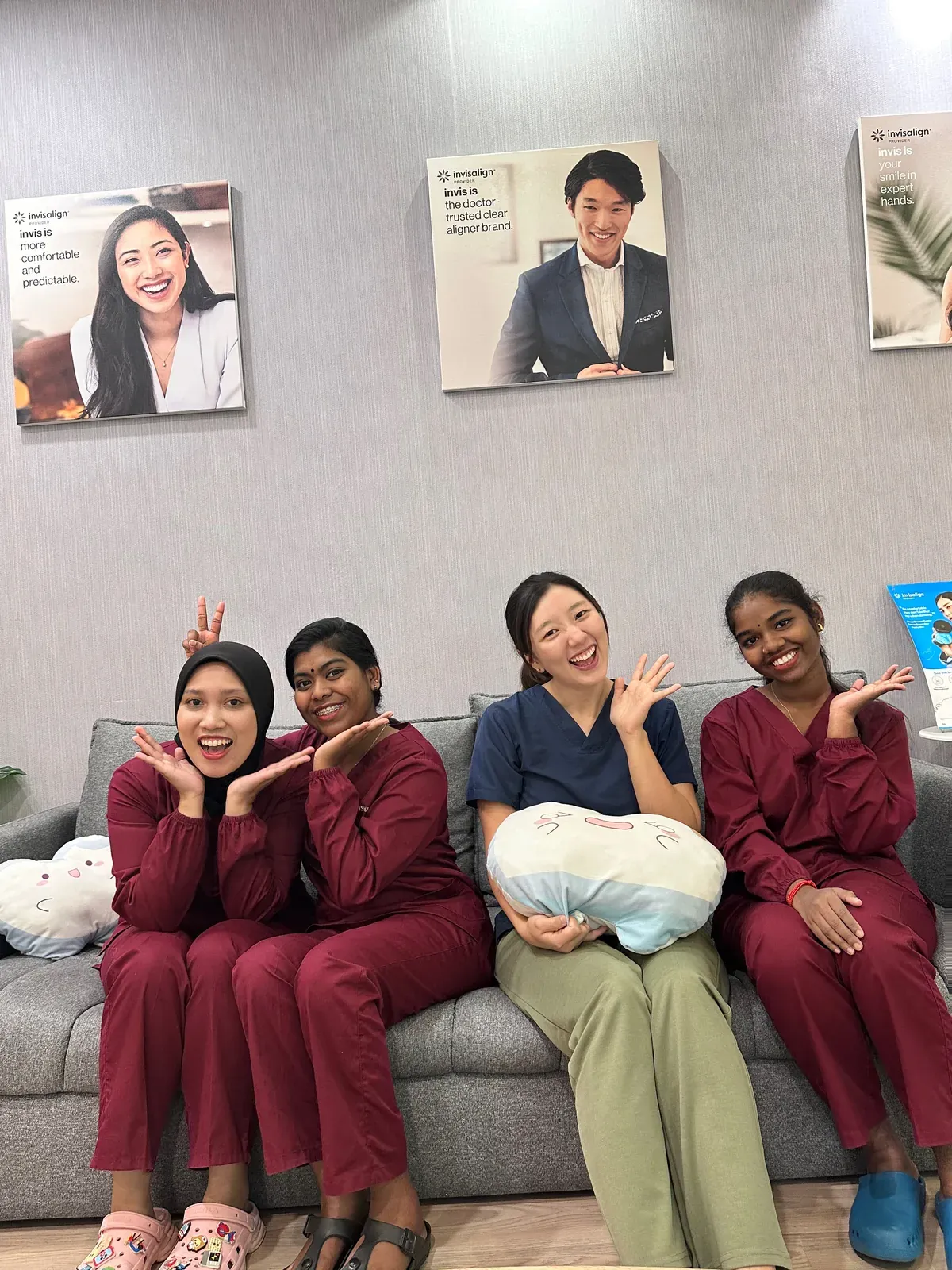 Four members of the Lau & Su Partners Dental team laughing on the waiting lounge sofa with tooth-shaped cushions in Bukit Jalil