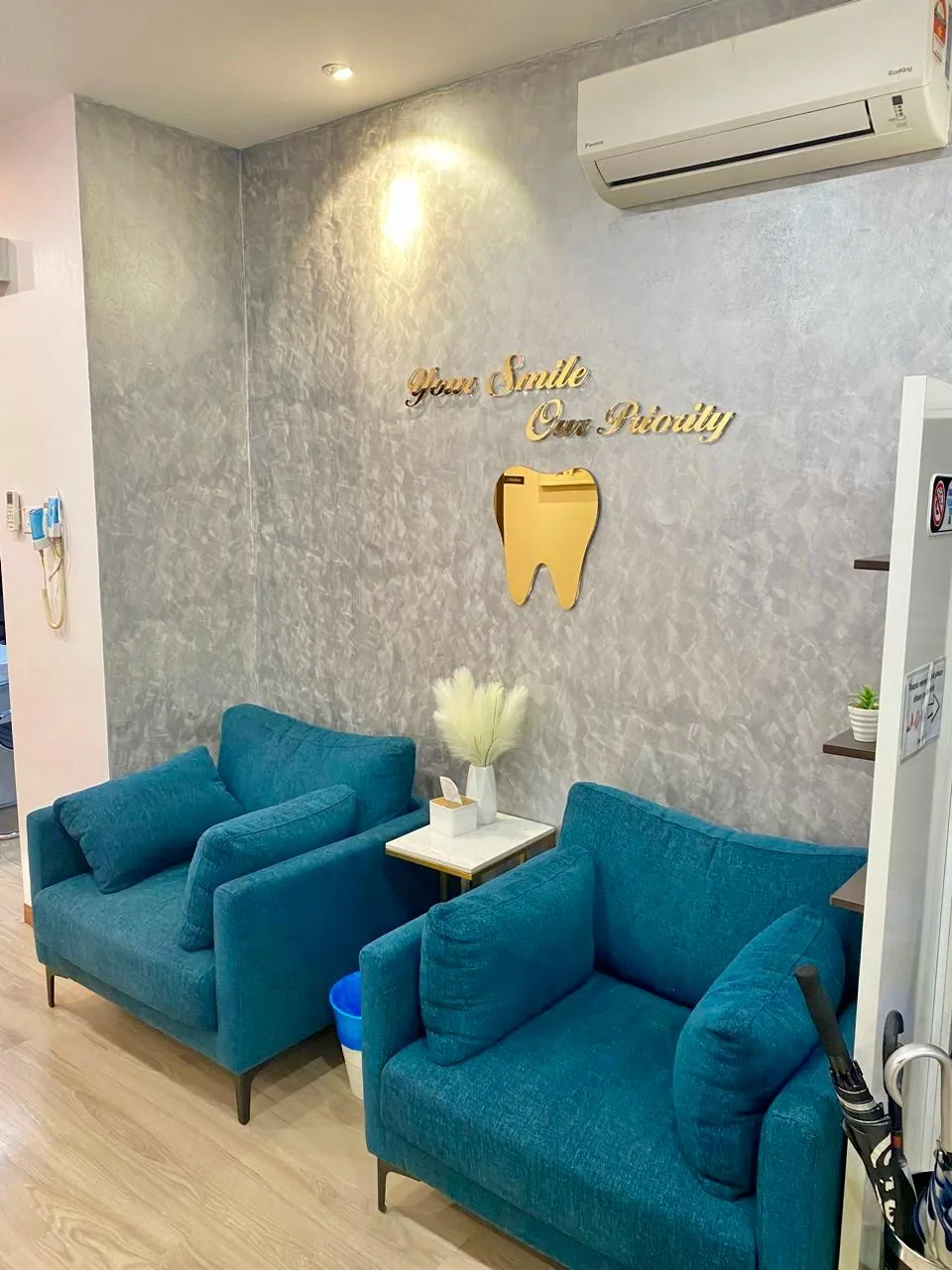Teal armchairs beneath the gold Your Smile Our Priority tooth feature wall in the Bukit Jalil dental clinic waiting area